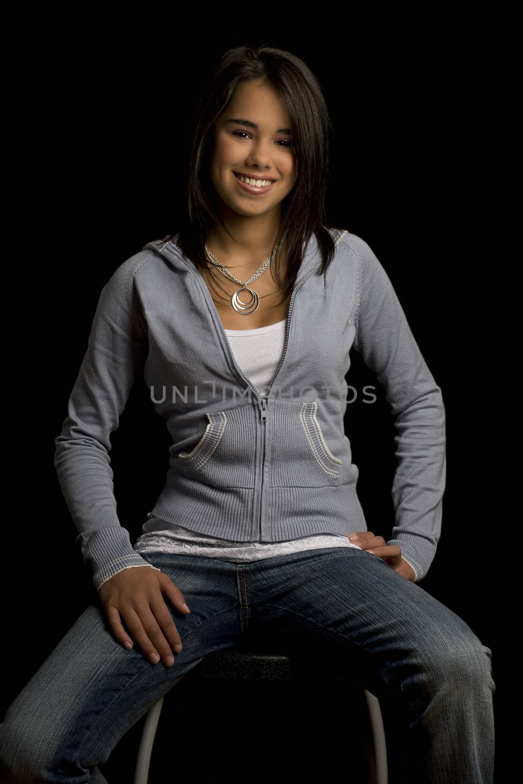 Teen girl sitting on a stool with great big smile against a black background