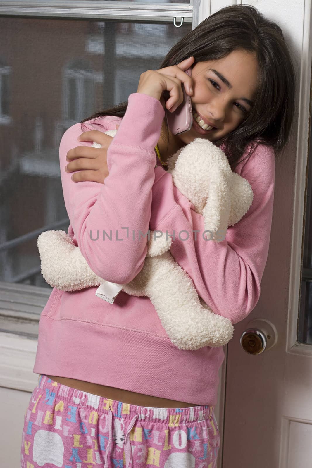 Teen girl in pink pajama hugging a teddy bear and talking on a cellphone