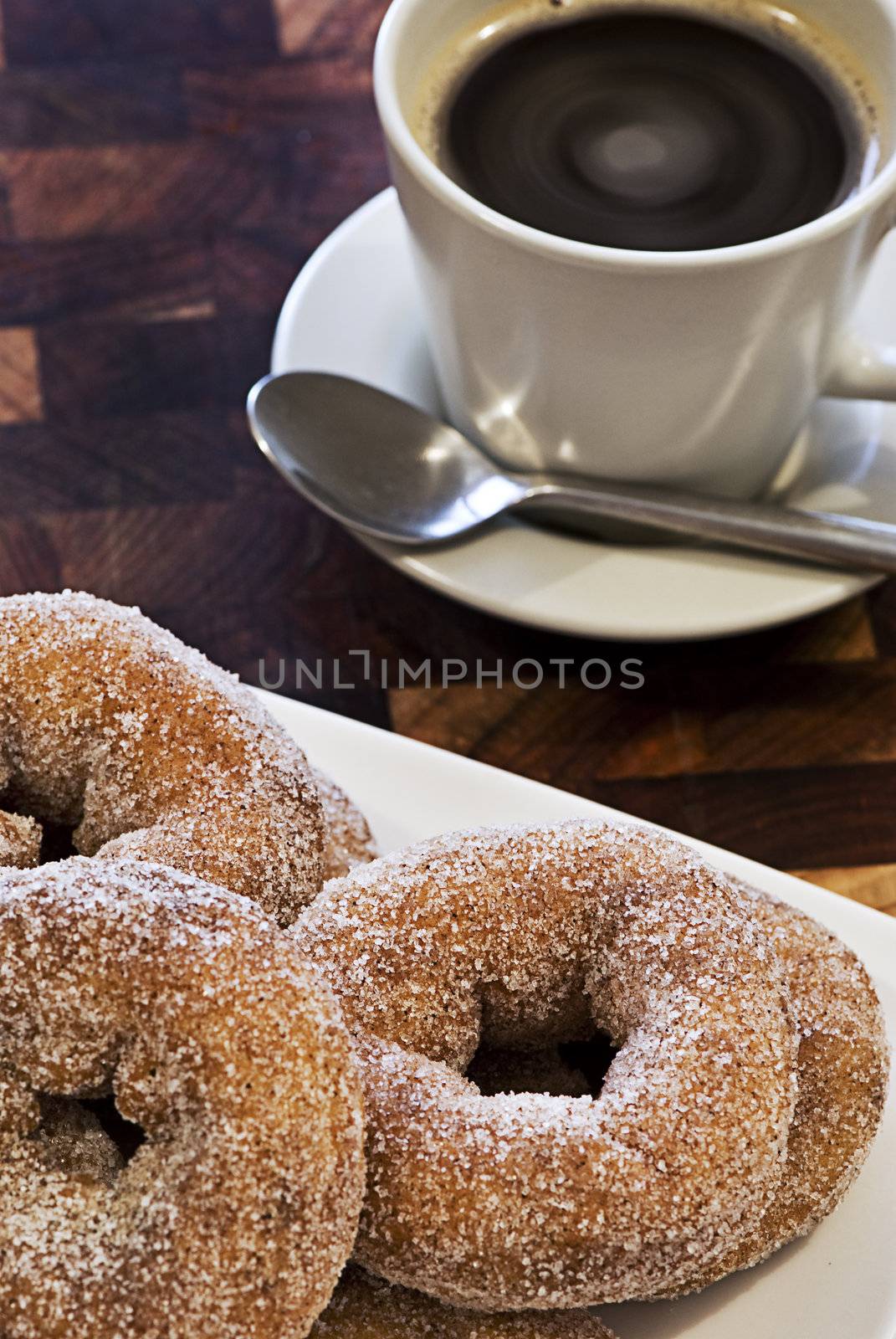A plate piled high with donuts in front of a hot cup of coffee.