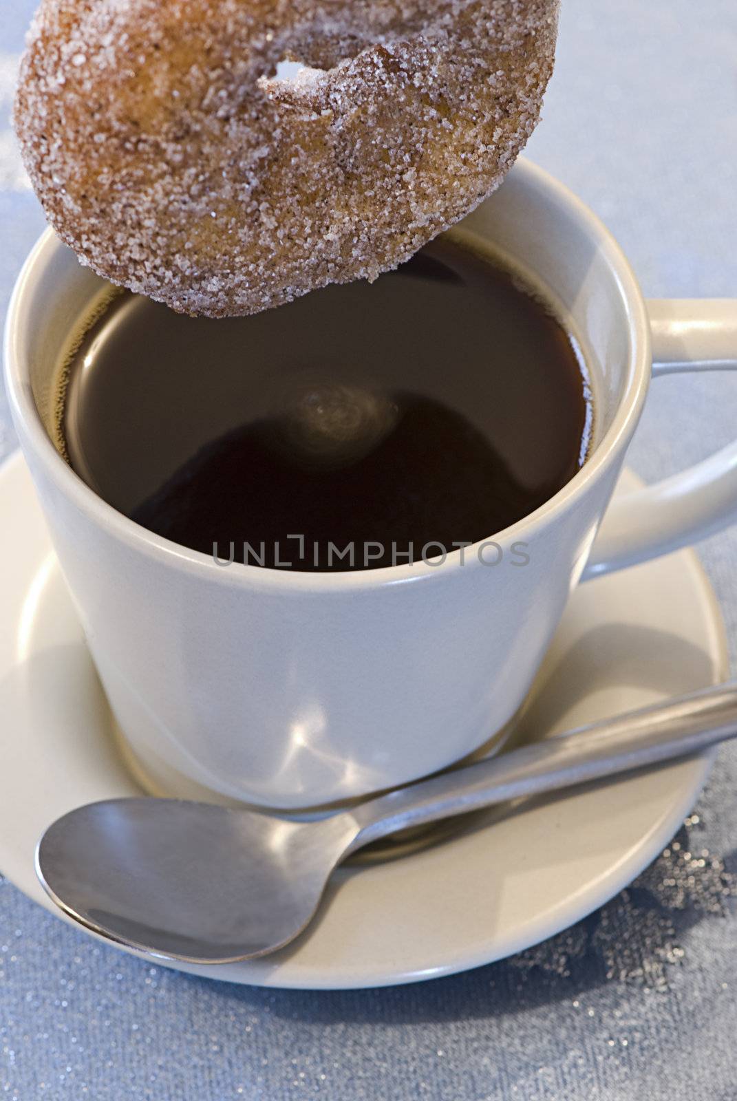 A cinnamon donut being dunked in a cup of coffee.