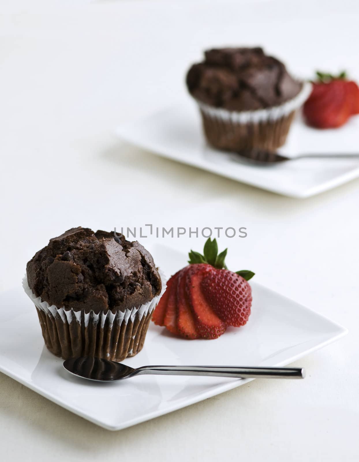 2 plates with chocolate muffins garnished with a strawberry.