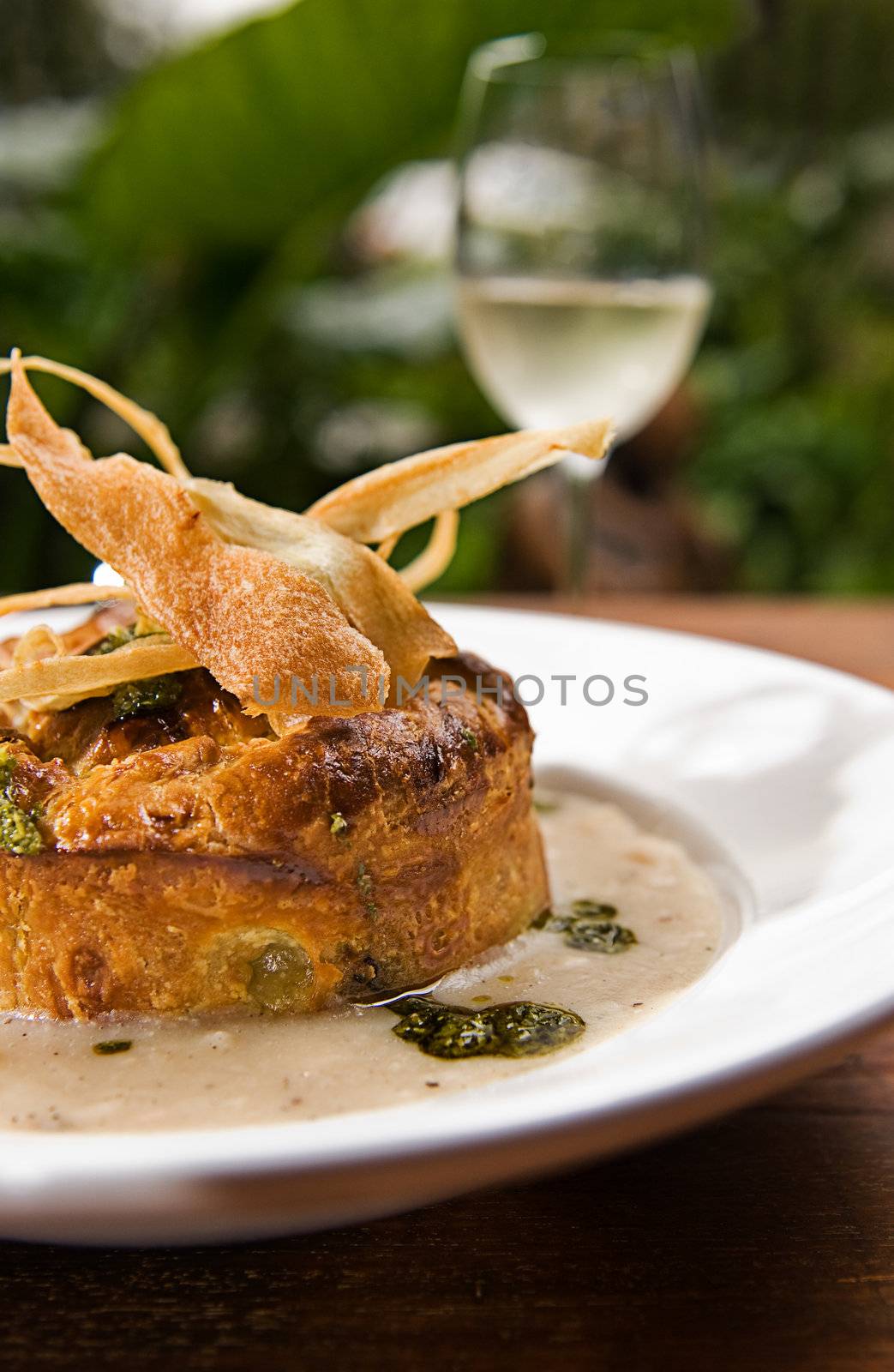 A pie with soup and garnish served with a white wine.