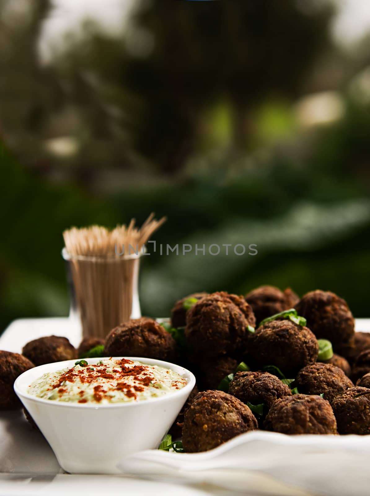 A platter of meatballs garnished with herbs, served on a platter with toothpicks and a dipping sauce.