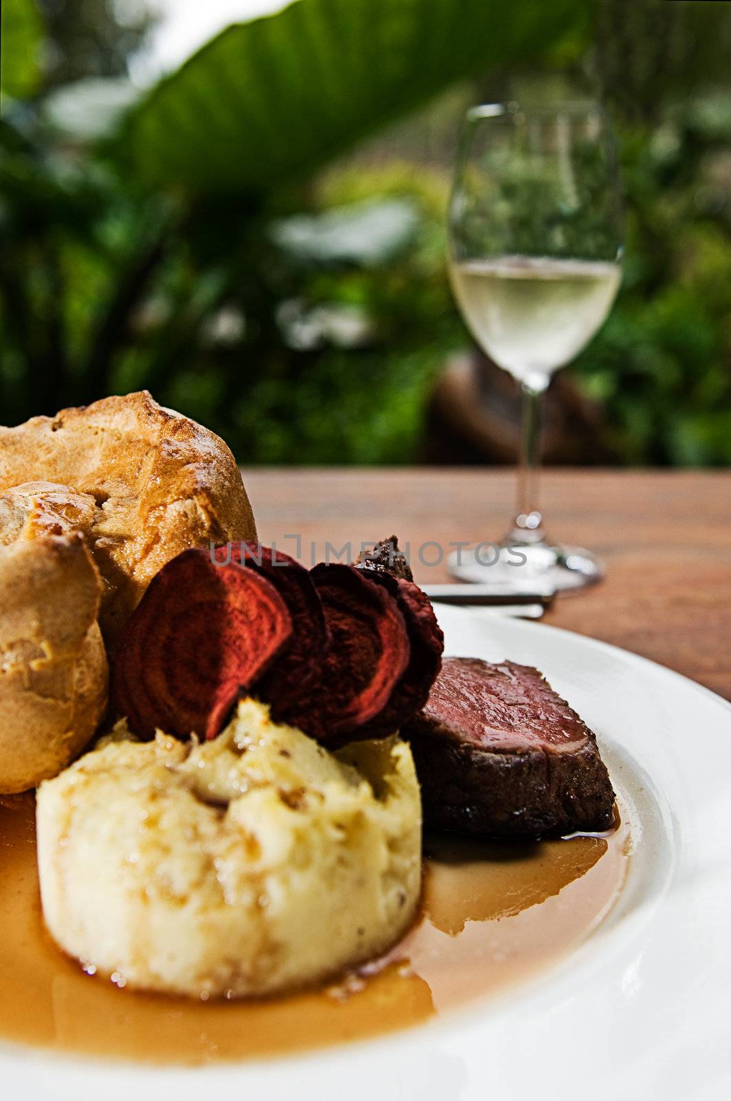 A roast beef with mash potato, yorkshire pudding, beetroot chips, gravy and a glass of white wine.