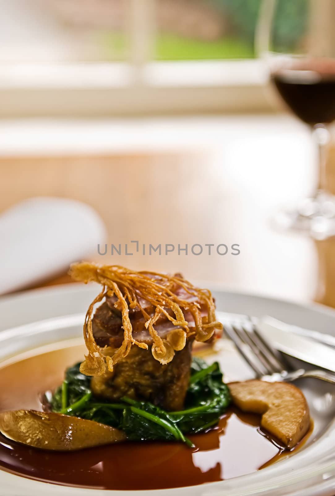 Crispy duck on a bed of spinach served with red wine in a restaurant.