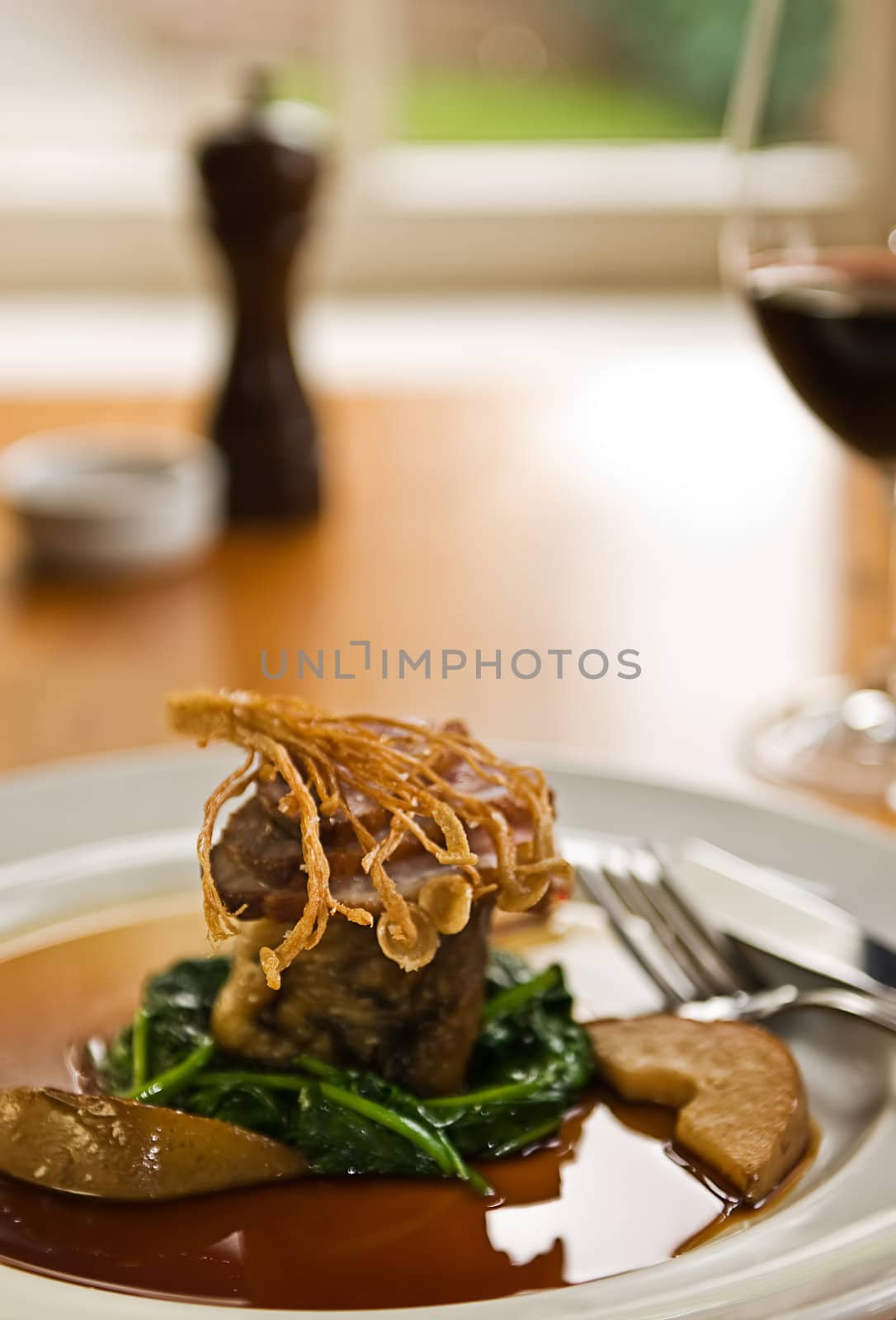 Crispy duck on a bed of spinach served with red wine in a restaurant.