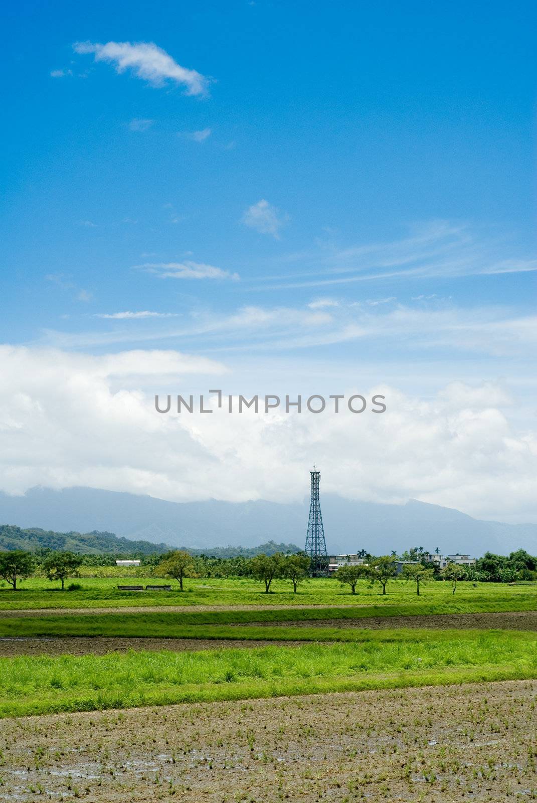 It is a tower on the green farm with blue sky.