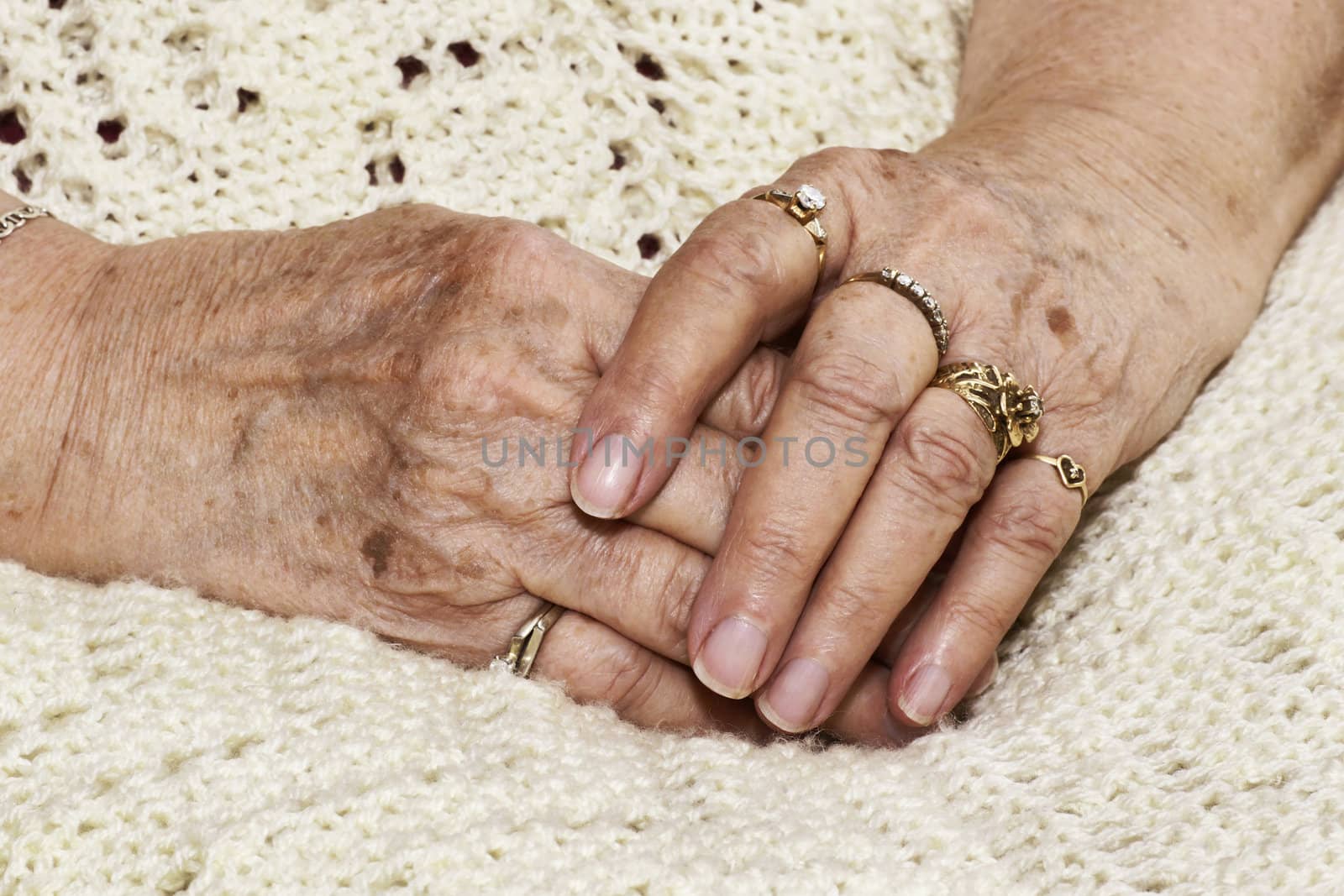 Senior woman's crossed hands with age spots over an off white knitted blanket, seems to be waiting.