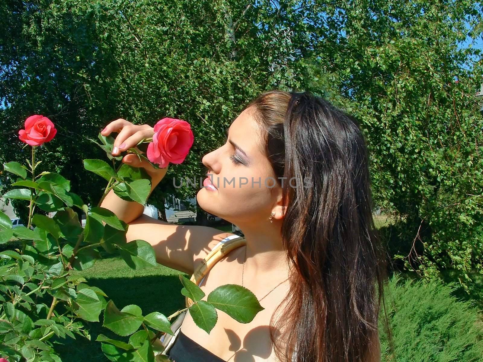 Young girl enjoys charming aroma of a rose in bright, a sunny day.