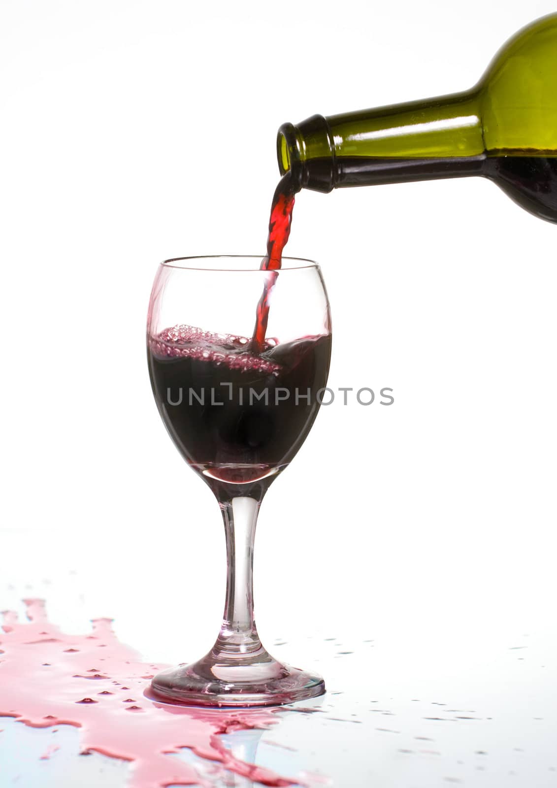Pouring delicious red wine in a glass with reflection and spill.