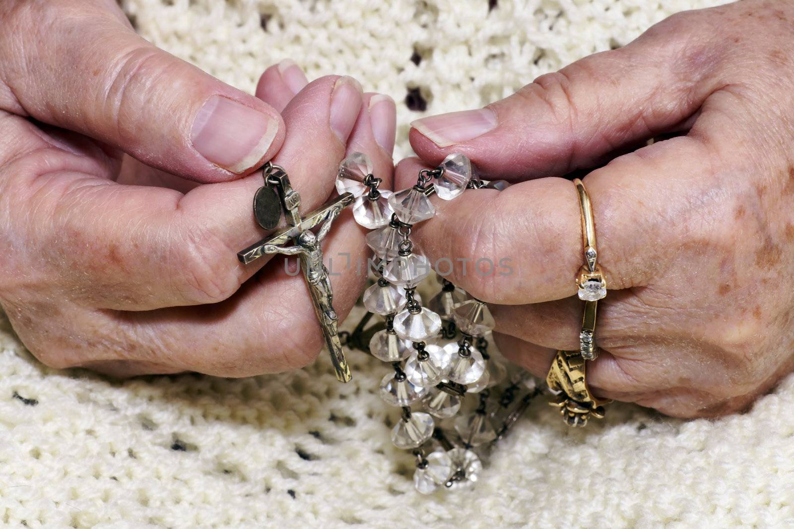 Hands of a senior woman holding a vintage crystal rosary to pray.