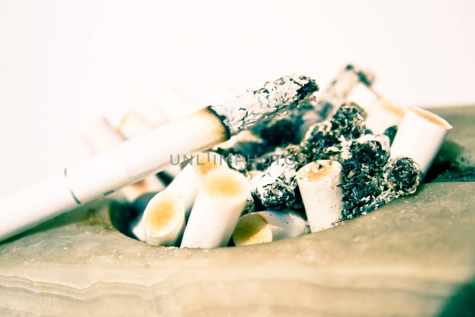 Close-up of a white stone square ashtray full of burnt cigarette butts