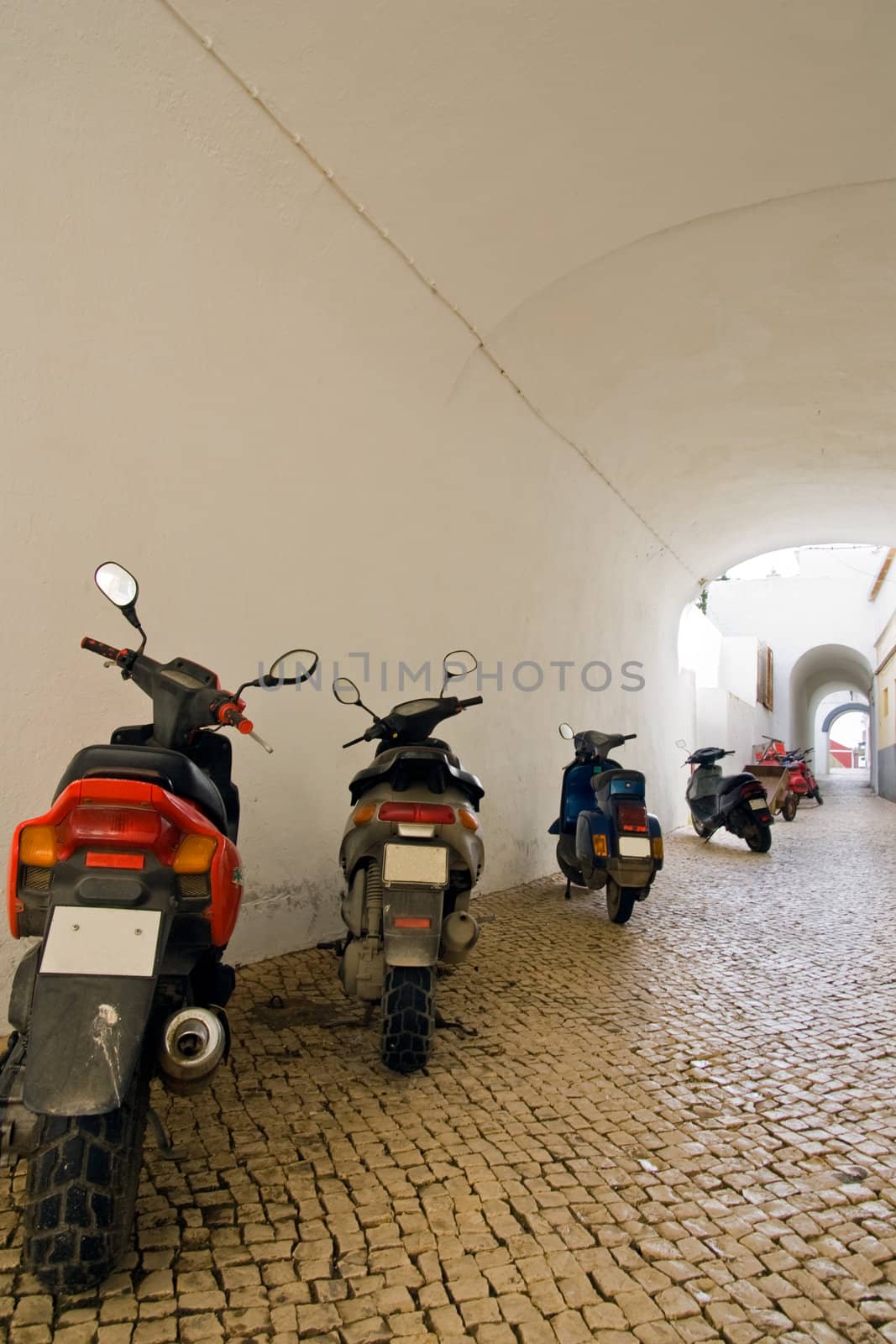 A line-up of motorcycles along a tunneled Portuguese street.