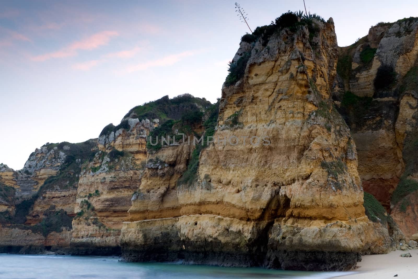 The sheer rocky cliffs at the beaches of 'Praia Dona Ana' in Lagos, Portugal, with a setting sunlit sky.