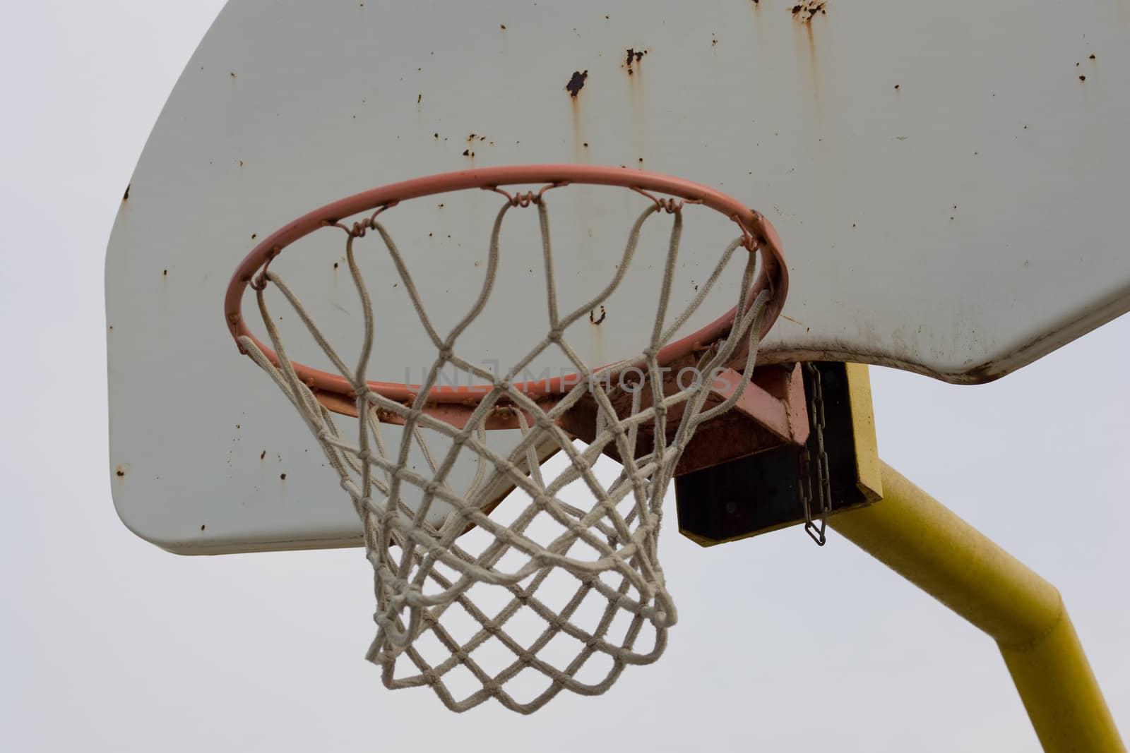 A closeup view of an old baketball net and backboard, isolated against a blue sky.