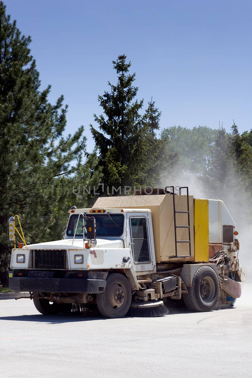 A street sweeper truck cleaning a parking lot with a dust cloud behind.