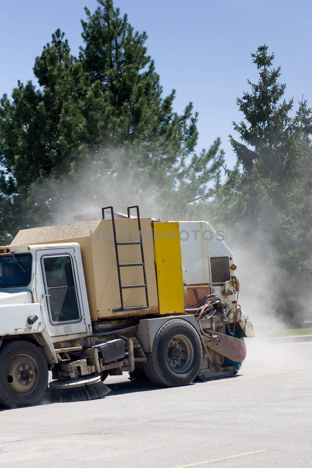 A street sweeper truck cleaning a parking lot with a dust cloud behind.