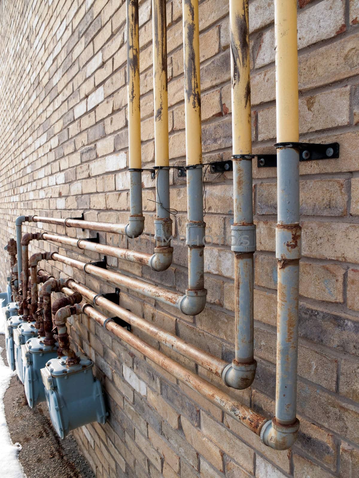 A bunch of natural gas pipes on the side of  a building, connected to meters.
