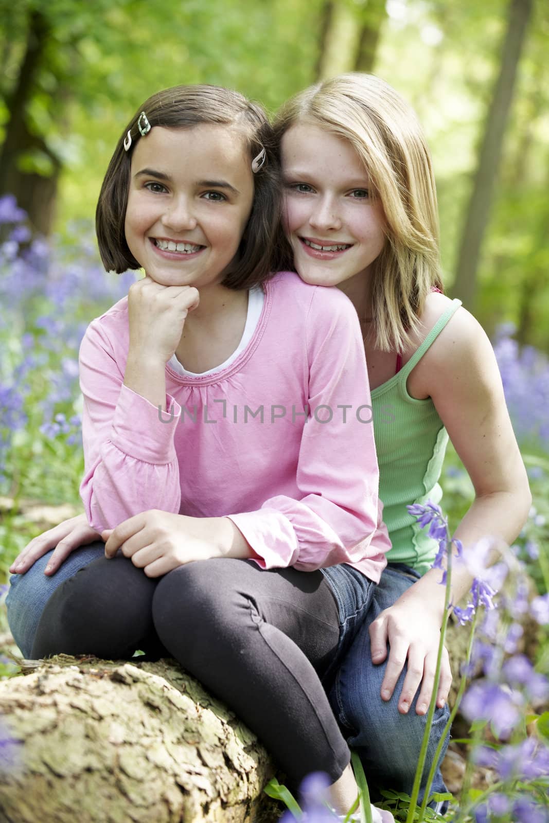 Two girls sitting together in a wood full of bluebells