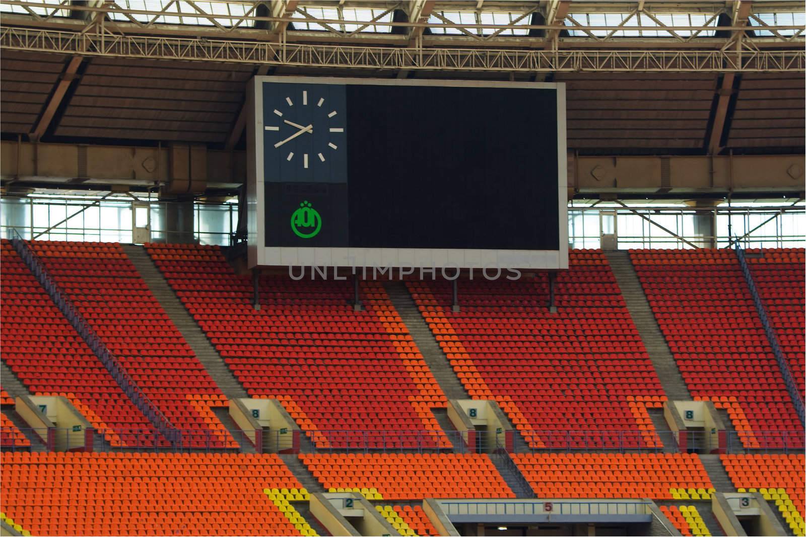 Rows of red and orange seats on the stadium with scoreboard displaying clock above them