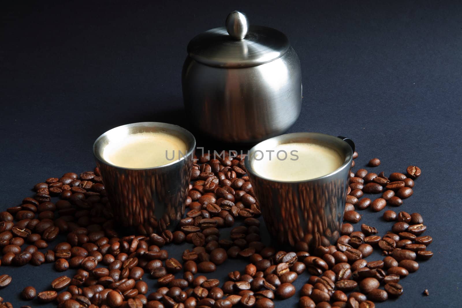 Coffee in metal cup with roasted beans on black background.