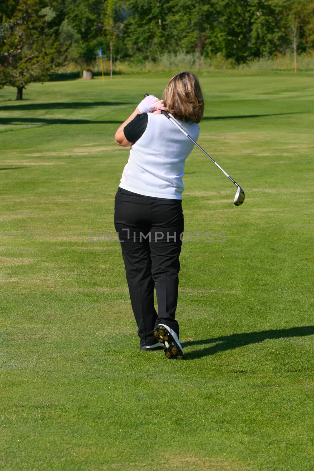 Blond female golfer following her shot from the fairway
