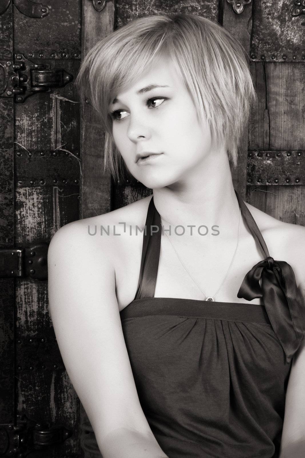 Beautiful blond sitting against an antique trunk with a serious expression