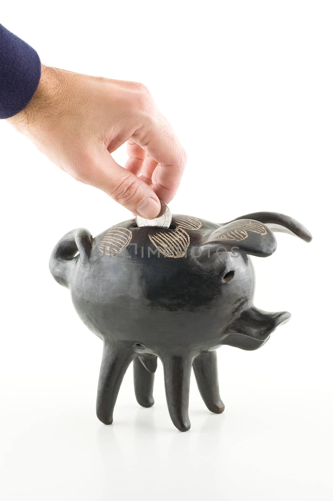 Male hand dropping a coin into a black piggy bank, white background.