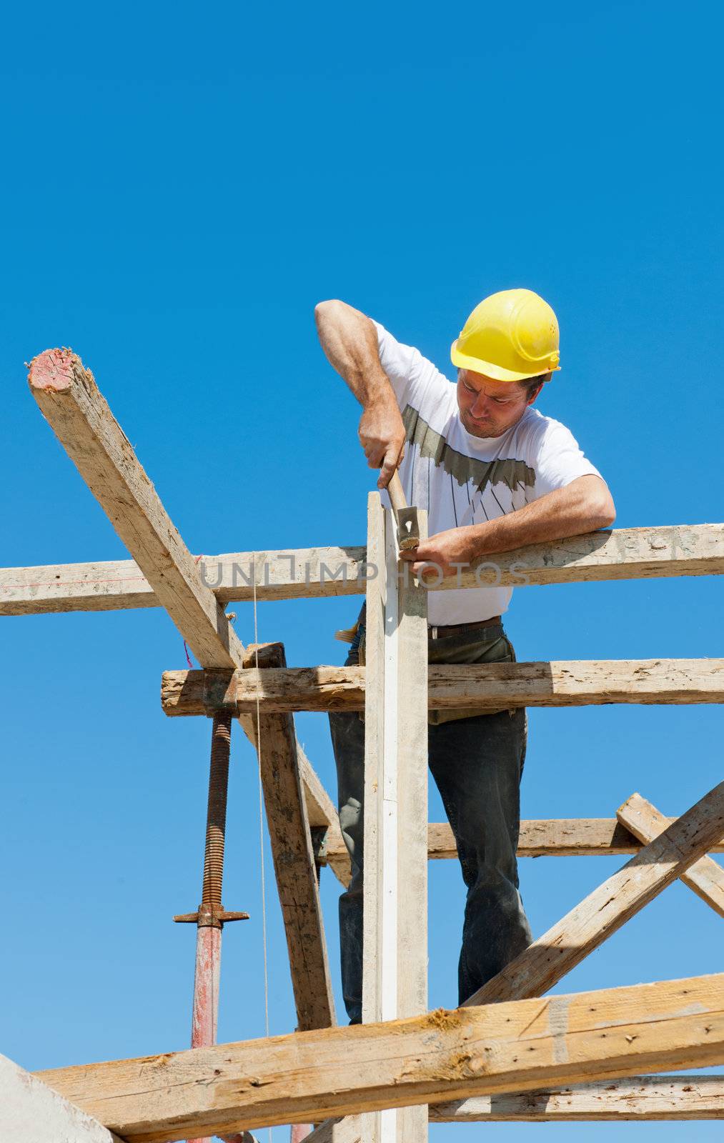 Authentic construction worker on scaffold, hammering nails on the wooden formwork of a construction site