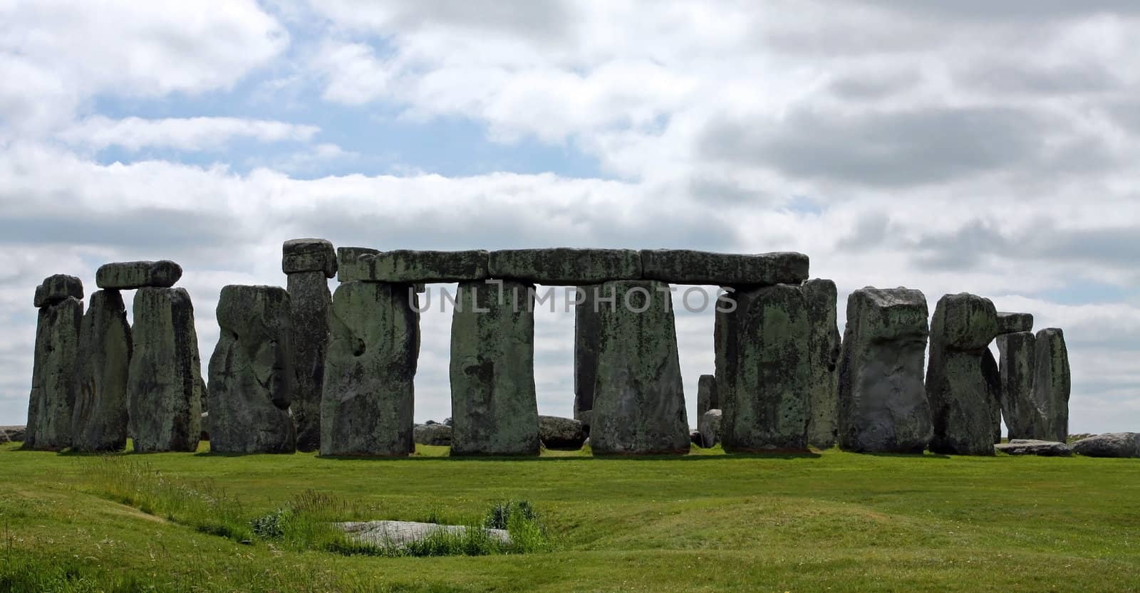 A view of England's Stonehenge against a blue sky and green grass.
