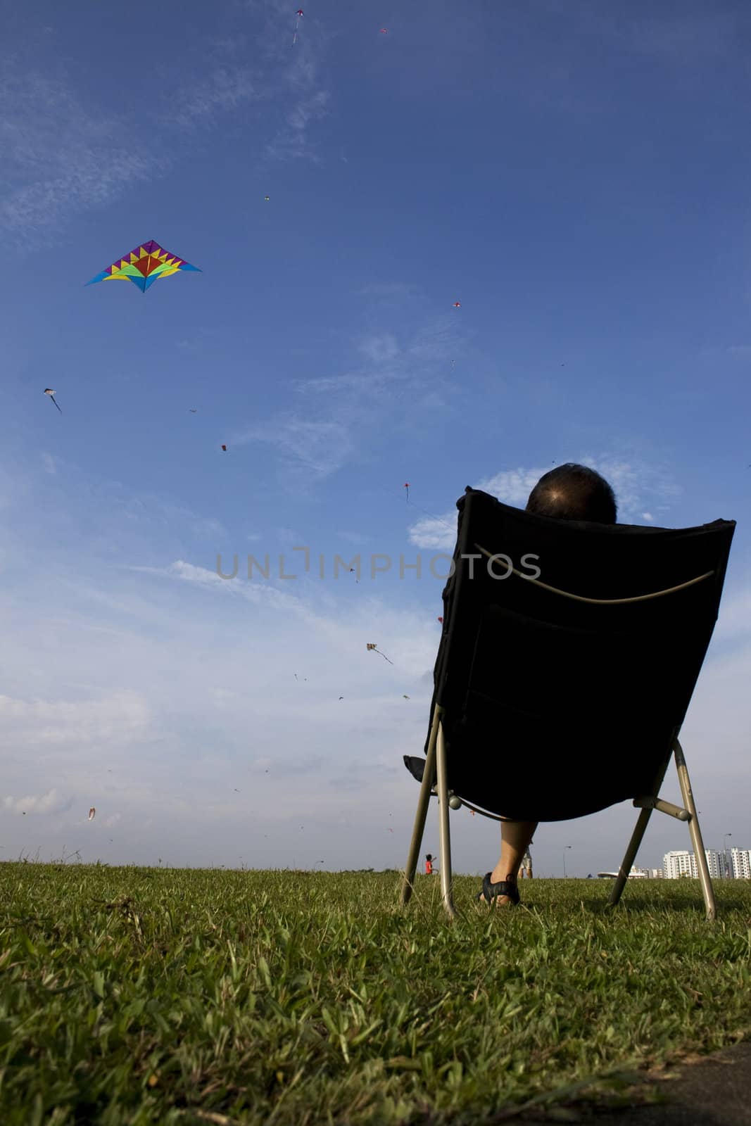 A man flying a kite wth a relax sitting position.