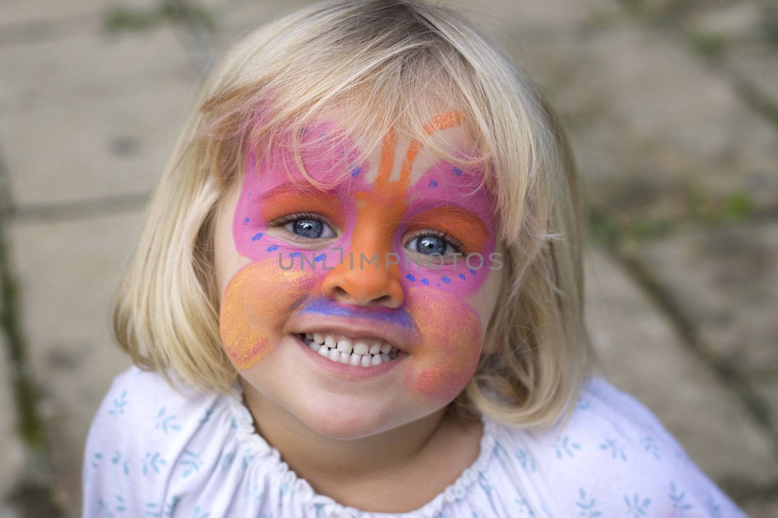 A 4 year old girl smiling at the camera with a butterfly painted over her face