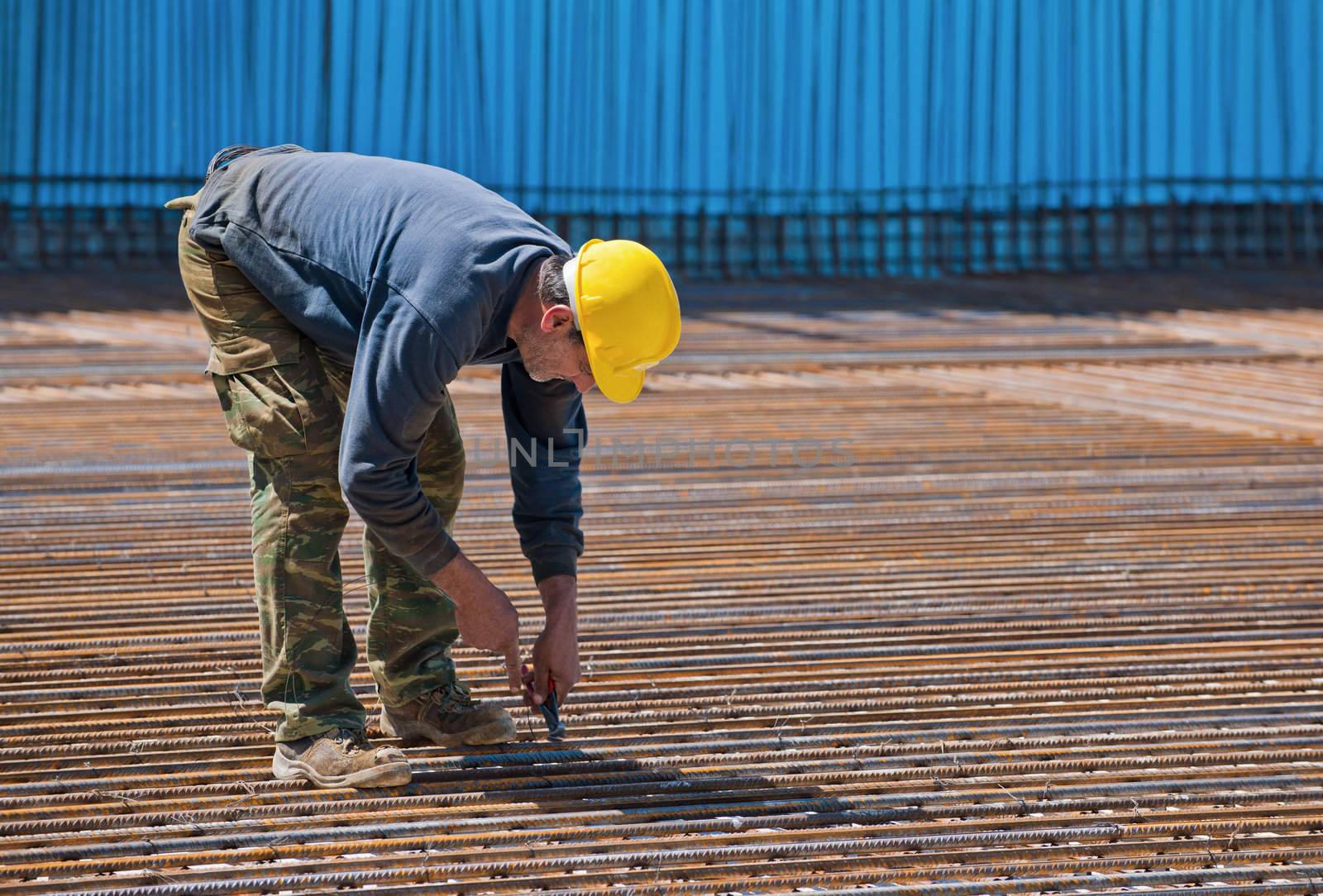 Authentic construction worker installing binding wires to reinforcement steel bars in construction site. Space for text.