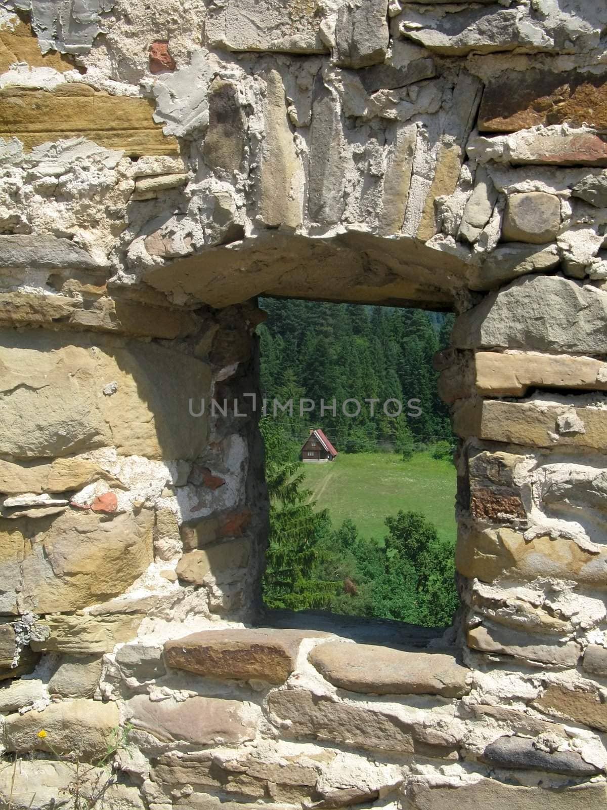 Window in a stone wall with view to forest and a small house. Castle in Stara Ljubovnya in Slovakia