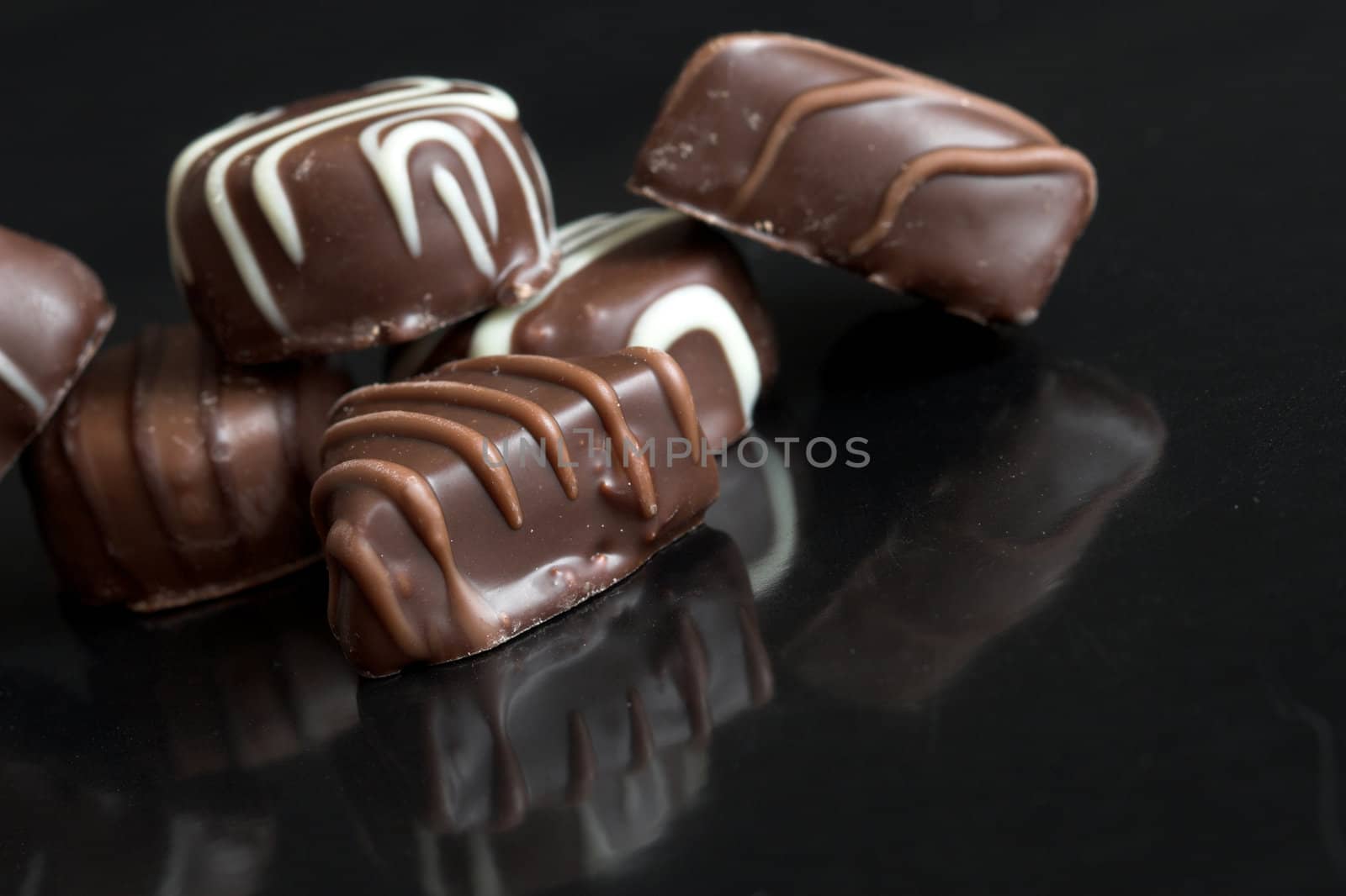 Delicious chocolates lying on black background with reflection