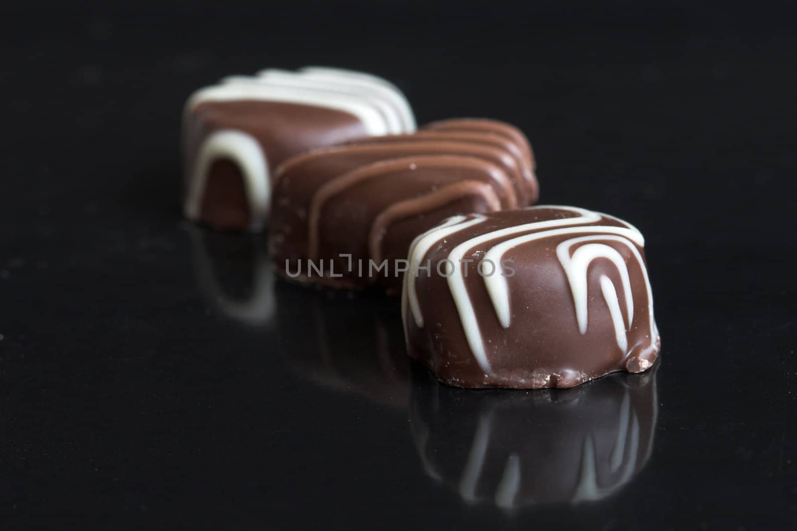 Three chocolates in a row on black background with reflection