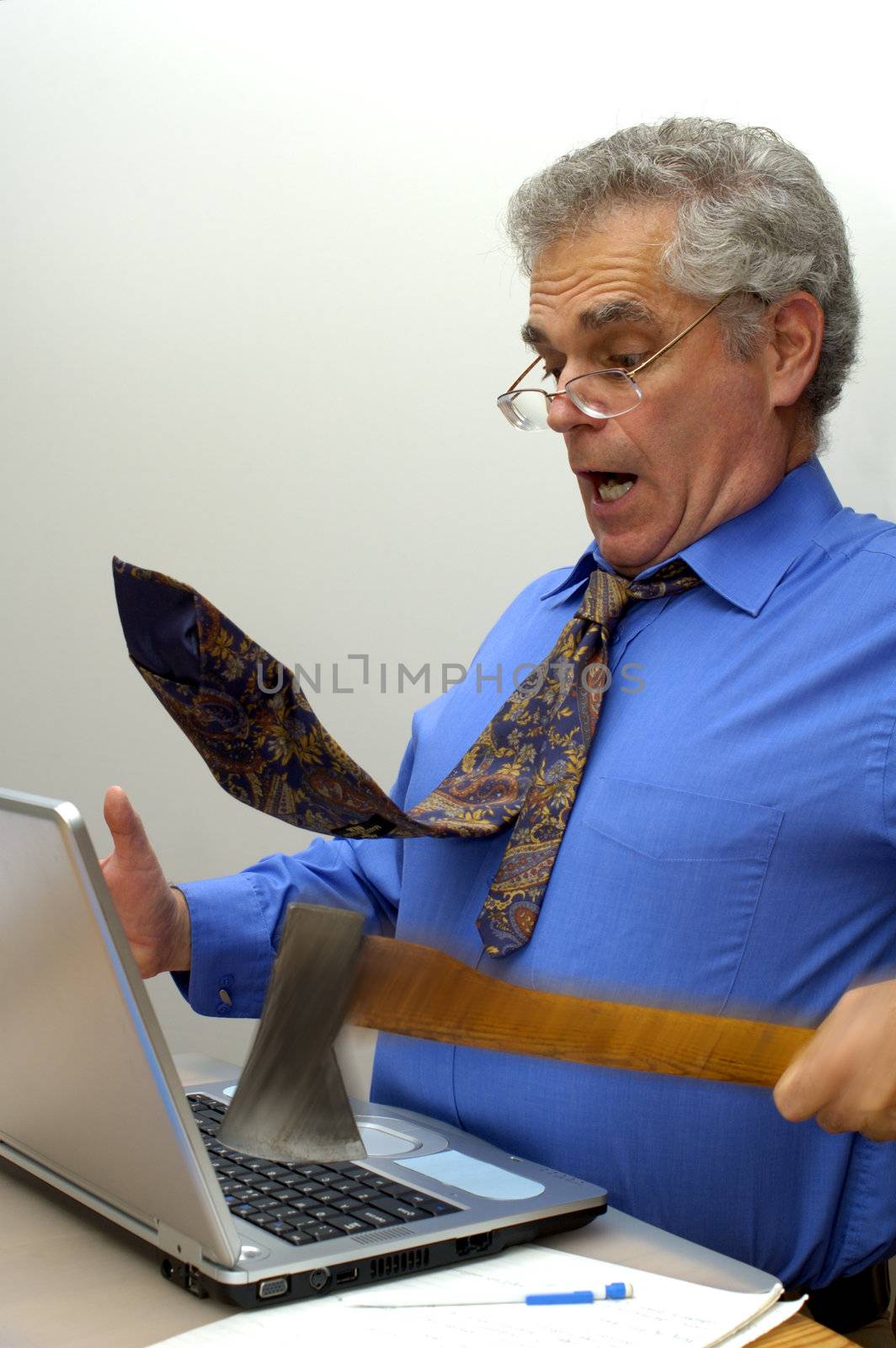 An older businessman fed up with his laptop, takes an axe to it. Motion blur on the axe and his hand. Space for text on the white background.