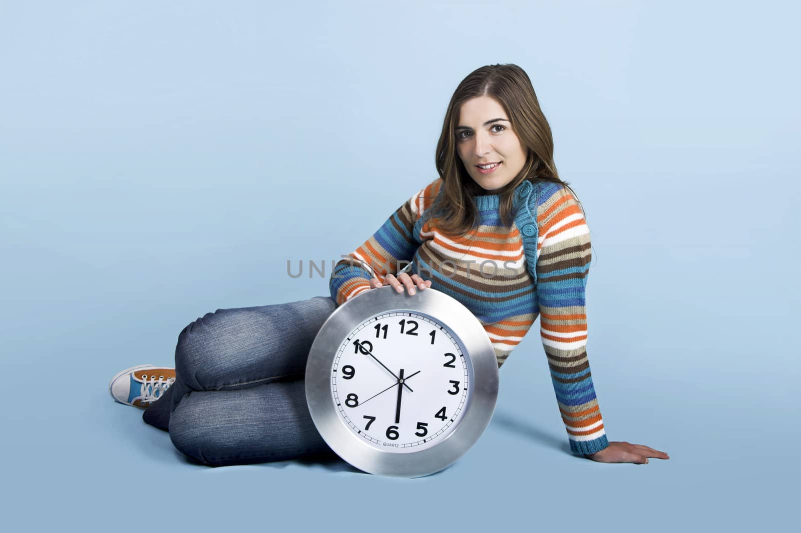 Beautiful woman seated on the ground holding a clock