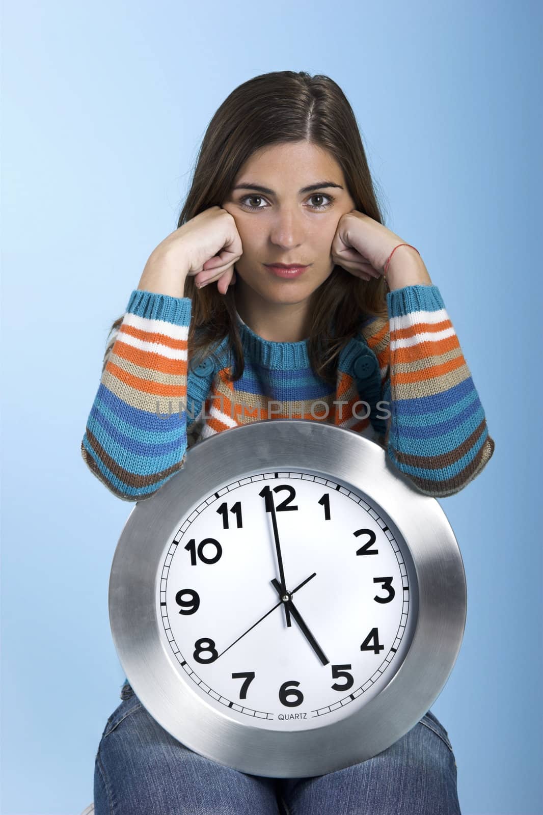 Beautiful women over knees holding a big clock in a blue background