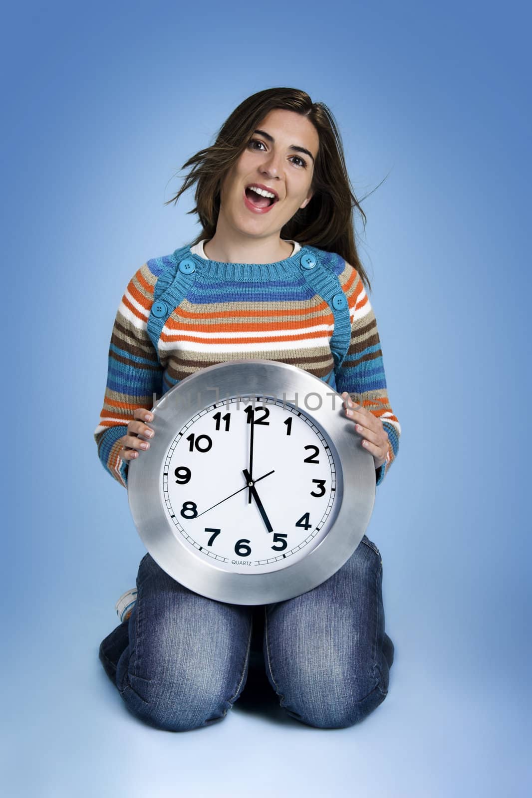 Beautiful women over knees holding a big clock in a blue background