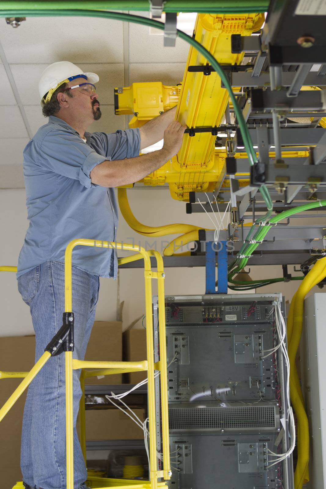 A telecommunication worker inspecting Fiberoptic cables in the fiberduct on a OSHA approved ladder.
