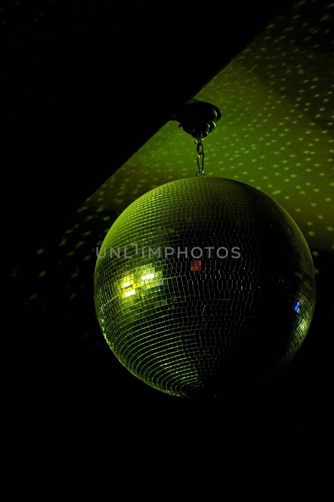 Disco ball in motion reflecting green light in night club with copy-space