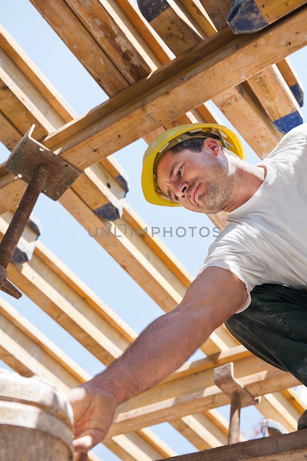 Authentic construction worker bending over under formwork girders to collect a bucket