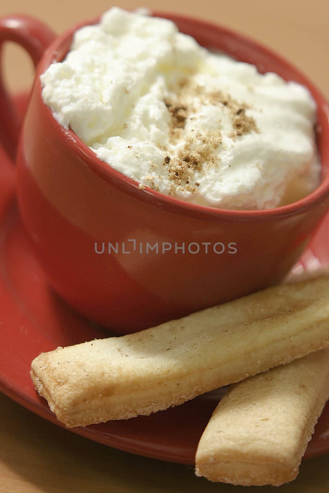 Coffee with whipped cream in a red cup on the saucer and the biscuits