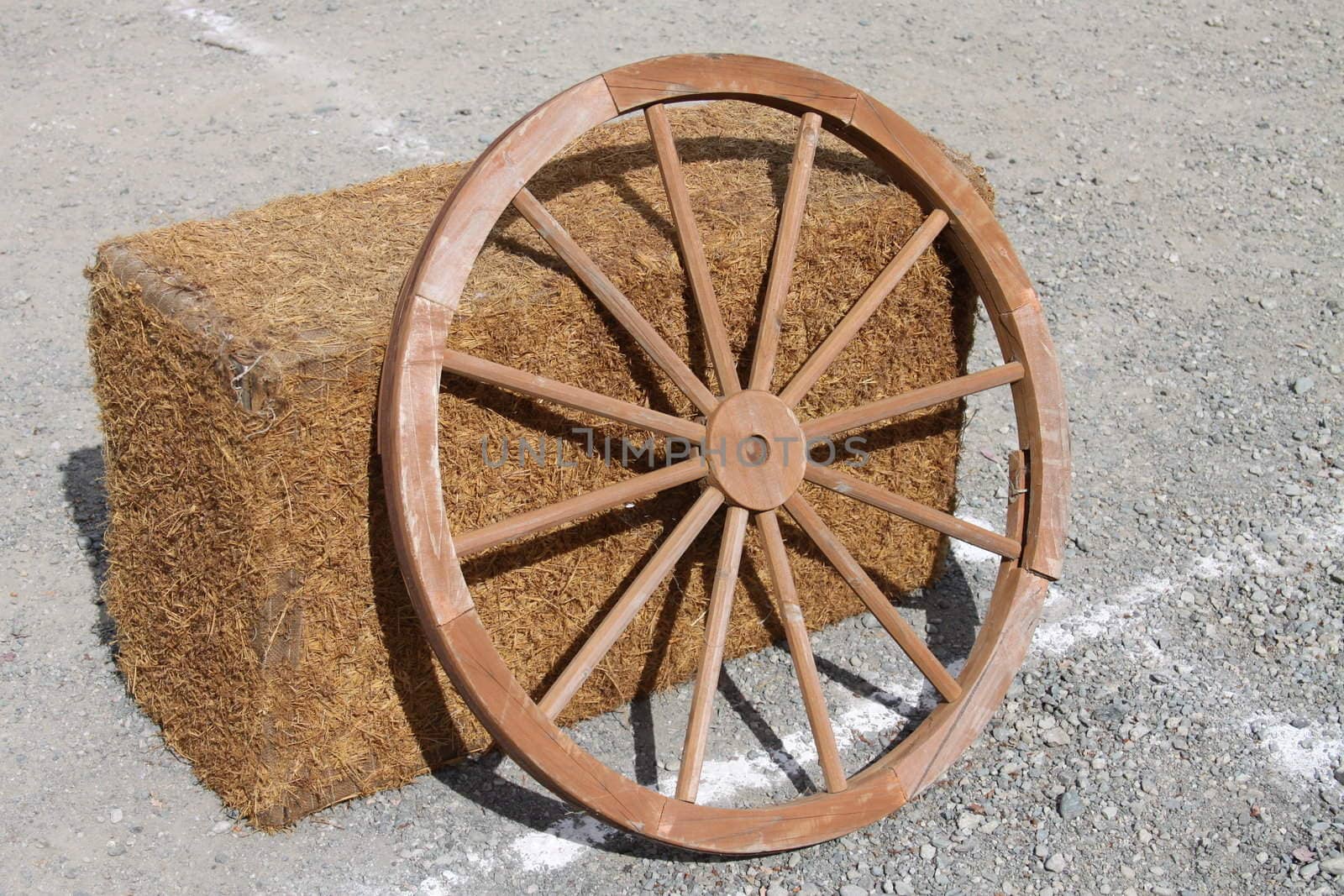 Wagon wheel next to a bale of hay.
