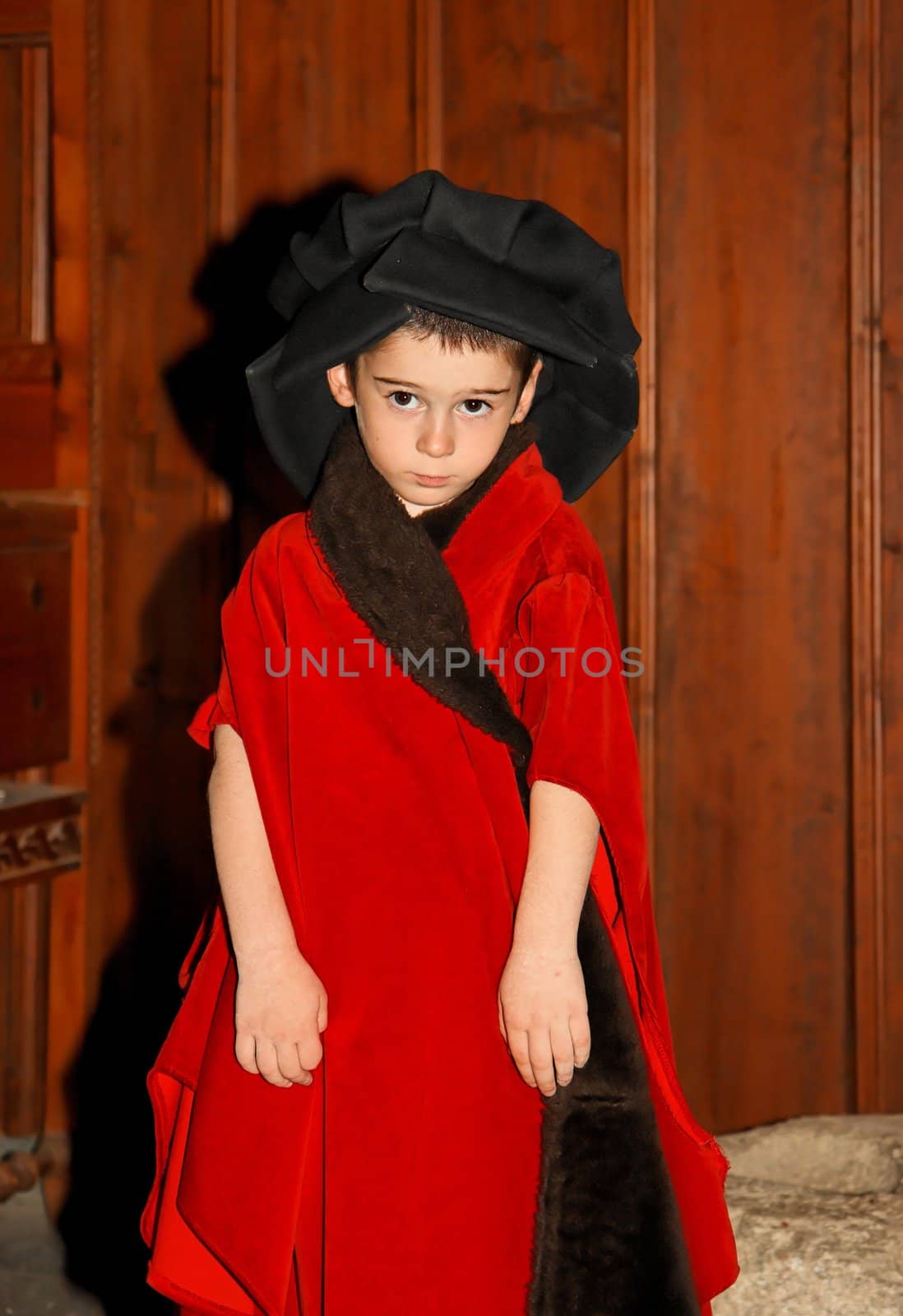 Serious cute little boy in medieval costume standing on wooden background