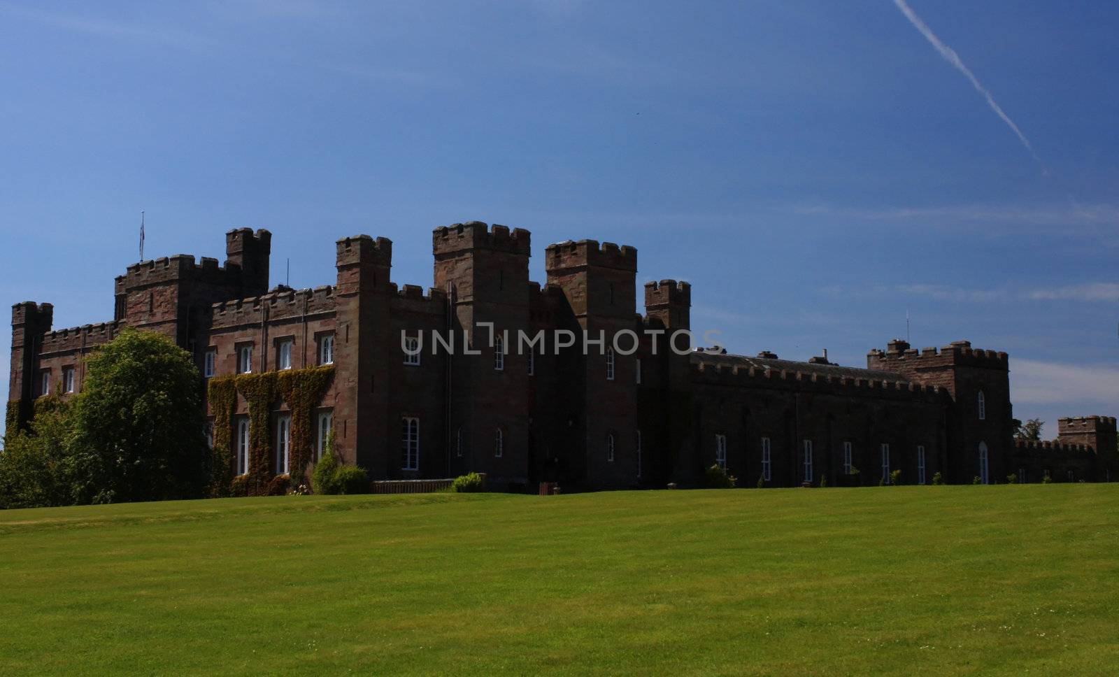 A view of Scone Palace in Perth, Scotland against green grass and a blue sky.
