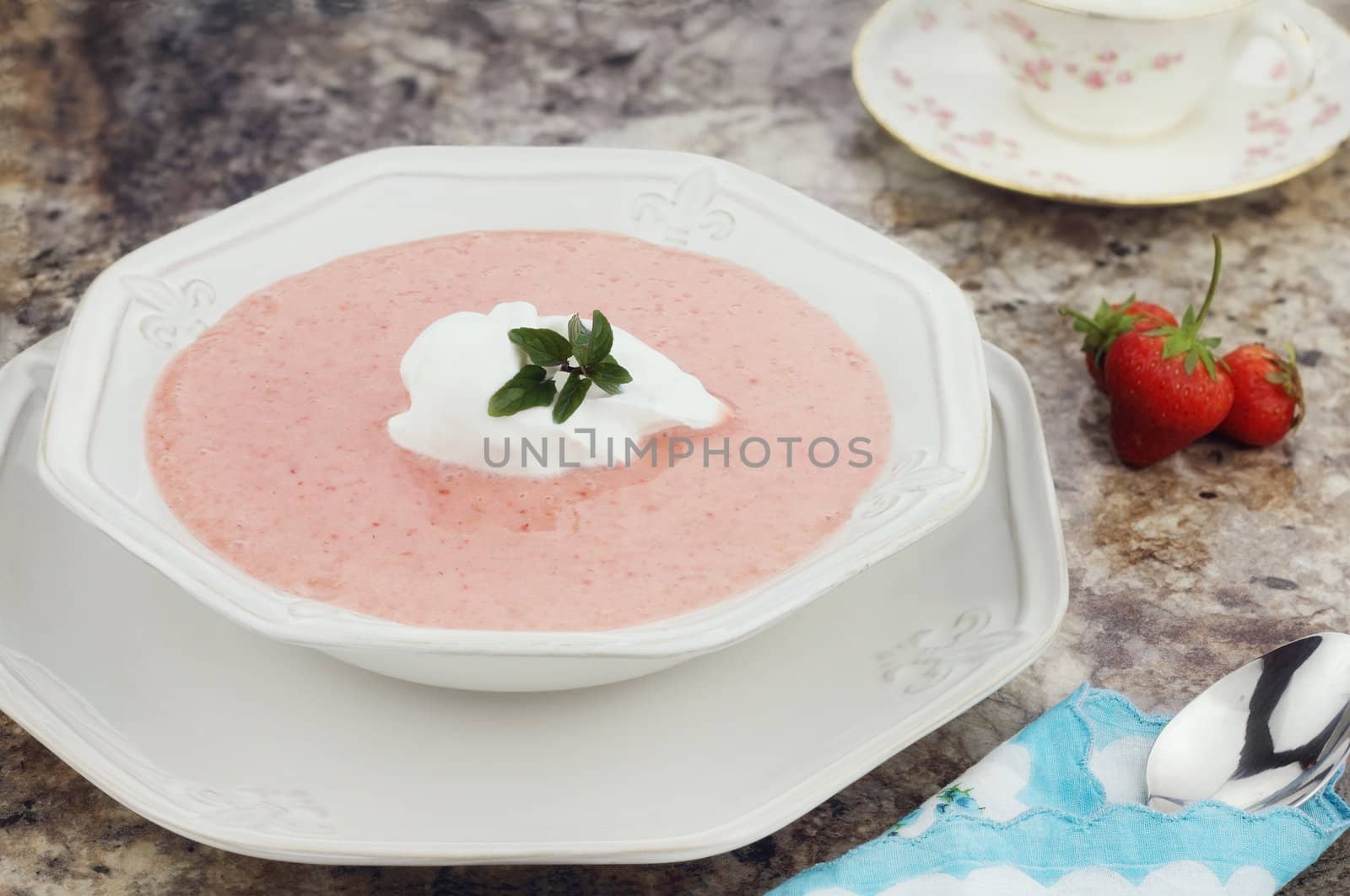 A bowl of chilled strawberry soup, garnished with a dollop of whipped cream and a fresh sprig of chocolate mint.

