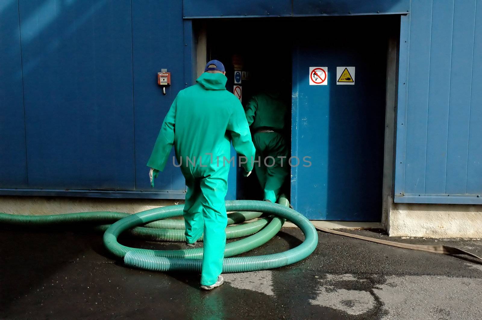 Two industrial workers wearing protection suits, entering the building. Vacuum tube on the ground.