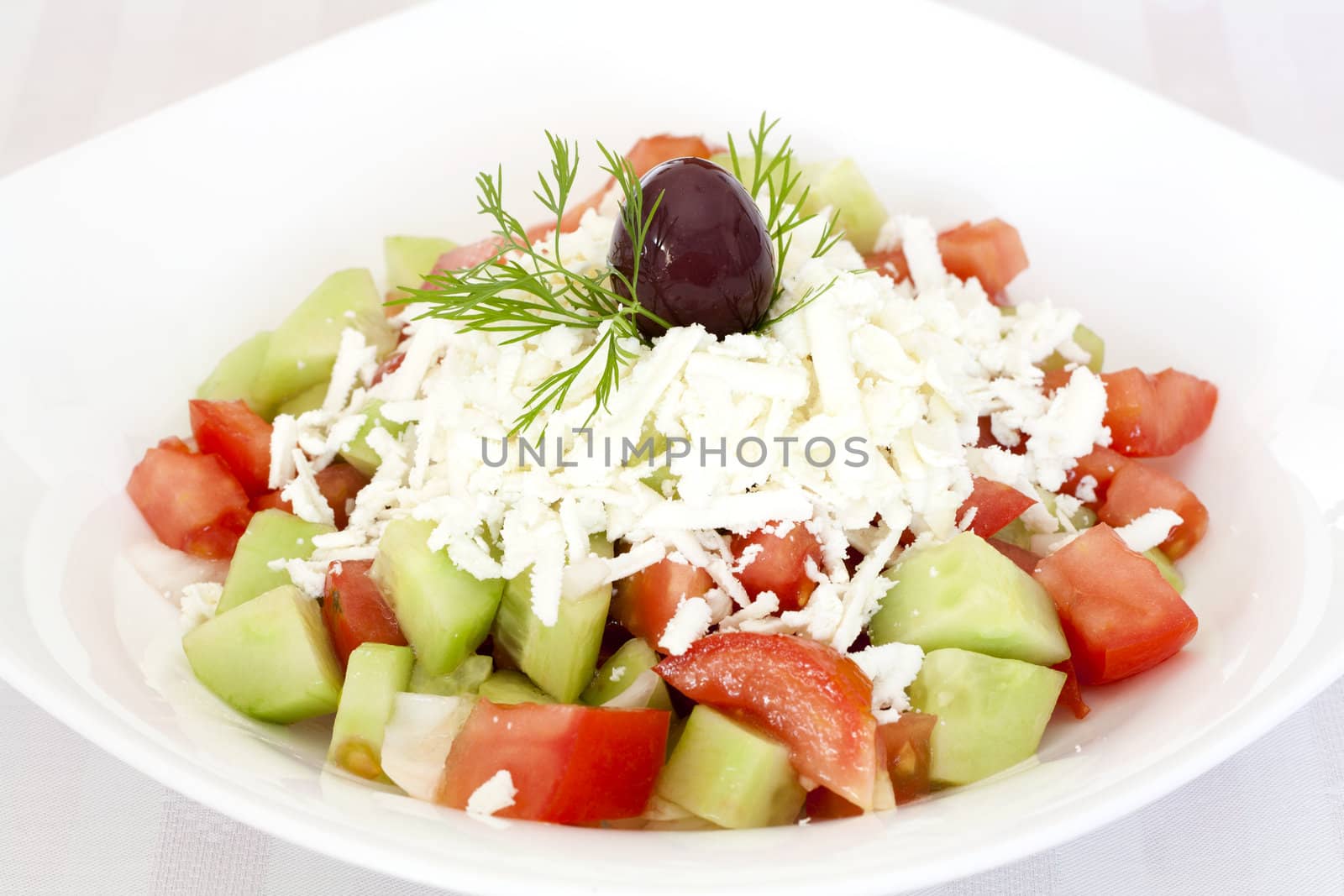 Fresh Greek salad with tomatoes, cucumber, onion, feta cheese and olive on top.